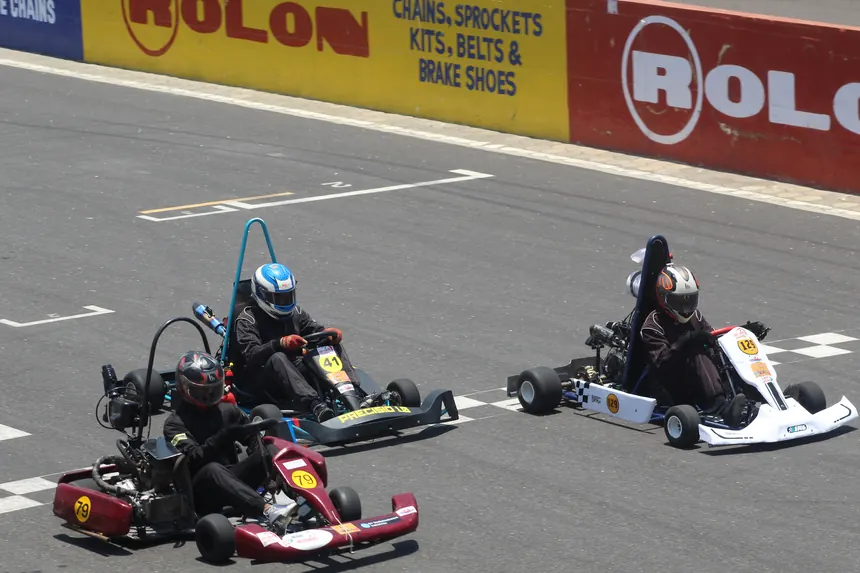 Three karts side by side on track in front of the trackside hoardings.
